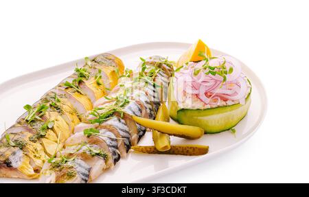 Tranches de maquereau fumé et salé décorées avec une sauce au pesto. Délicieuse entrée de rillettes de poisson servie avec du concombre et des oignons. Banque D'Images