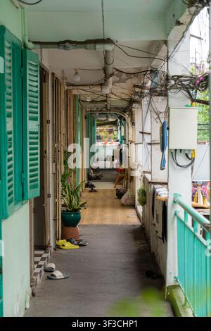 Un couloir étroit commun dans un vieil immeuble de la rue Nguyen Thien Thuat, montrant des murs érodés, un câblage dense, des volets verts, une plante en pot Banque D'Images