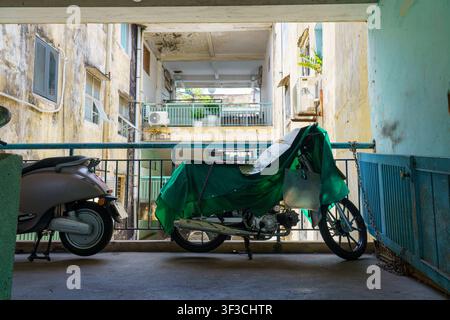 Une moto couverte repose dans un couloir étroit d'un vieil immeuble délabré de la rue Nguyen Thien Thuat à Saïgon, au Vietnam. Banque D'Images
