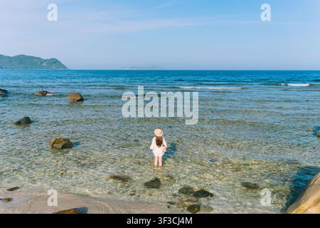Femme debout dans une eau peu profonde de la mer avec des rochers et une île au loin Banque D'Images