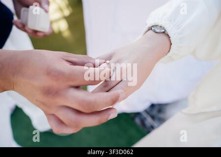 Homme mettant une bague de fiançailles en diamant doré au doigt d'une femme lors d'une demande en mariage romantique, un tendre gros plan du moment des fiançailles Banque D'Images