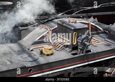 La vapeur s'élève d'une locomotive noire avec des tuyaux en cuivre et des composants en laiton. Pièces mécaniques visibles et saleté. Banque D'Images