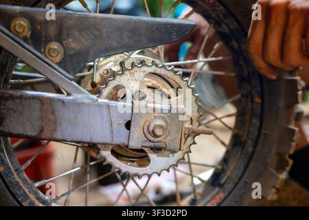 Un pignon arrière et une chaîne de moto rouillés en cours d'ajustement lors de la réparation dans l'atelier, un gros plan granuleux montrant l'usure du métal, les détails de la main et de la roue sont transmis Banque D'Images