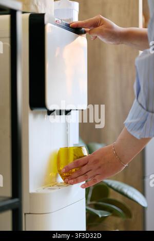 Femme adulte remplissant un verre à boire au distributeur d'eau du bureau Banque D'Images