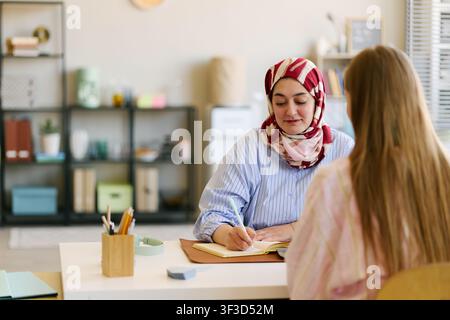 Femme adulte musulmane prenant des notes lors d'une consultation client Banque D'Images