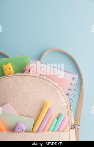 Ouverture d'un sac à dos révélant une collection de cahiers aux couleurs pastel, des stylos, des surligneurs, des notes adhésives et des gommes, symbolisant l'éducation, la créativité, Banque D'Images