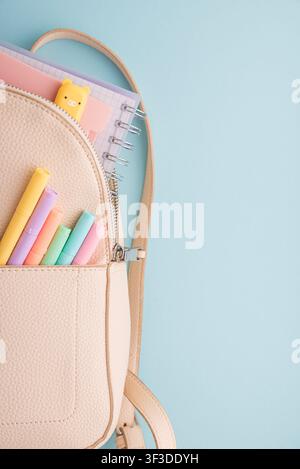 Ouverture du sac à dos révélant des cahiers à spirale et un charmant effaceur en forme de cochon, avec une poche avant contenant une collection de marqueurs pastel colorés, tout Banque D'Images