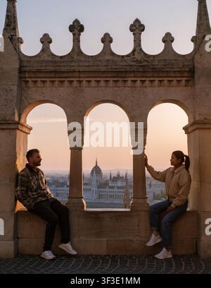 Budapest, Hongrie offre une vue imprenable au coucher du soleil depuis la Bastion des pêcheurs, où un couple capture le moment. L'architecture complexe encadre leur r Banque D'Images