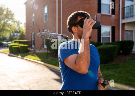 Un homme en chemise bleue manœuvre un drone volant à l'aide d'une télécommande tout en portant des lunettes de réalité virtuelle Banque D'Images