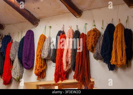 Écheveaux de laine et de fil d'alpaga colorés teints à la main suspendus à un mur en plâtre rustique dans un atelier de tissage textile traditionnel au Pérou. Banque D'Images