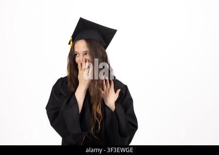 Jeune diplômée portant une coiffe académique ajustant son manteau et tenant son diplôme Banque D'Images