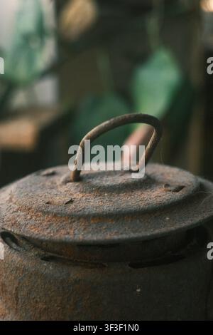 Photo macro rapprochée d'un couvercle métallique vintage fortement rouillé avec une poignée en fil de fer, sur un fond doux et flou de feuillage vert Banque D'Images