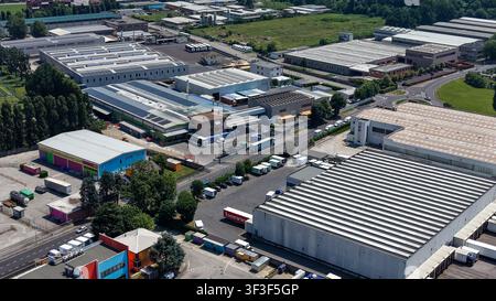 Vue aérienne d'un parc industriel commercial et d'un centre logistique avec de grands entrepôts, des quais de chargement, des camions et des routes d'accès pavées à Tribiano, Lombardie Banque D'Images