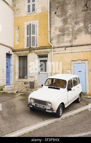 Une voiture classique Renault 4 blanche vintage garée dans une rue calme devant des maisons en pierre historiques aux volets bleus à Arles, France. Banque D'Images