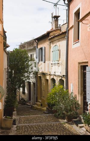 Des plantes en pot bordent la rue Ernest Renan, une étroite ruelle pavée entourée de bâtiments résidentiels historiques aux teintes pastel à Arles, en France. Banque D'Images