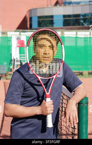 Joueur de tennis masculin tenant une raquette devant son visage sur un court de tennis en terre battue Banque D'Images