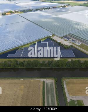 Vue aérienne d'un champ solaire flottant sur un étang entouré de grandes serres en verre et de champs agricoles aux Pays-Bas. Banque D'Images