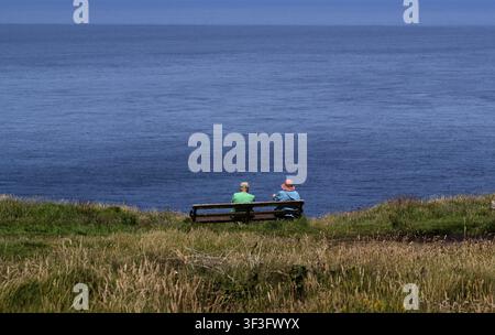 Couple âgé, homme, femme, assis sur un banc en train de regarder la mer, côte, St Just in Penwith, Cornouailles, Angleterre, Grande-Bretagne, Grande-Bretagne Banque D'Images