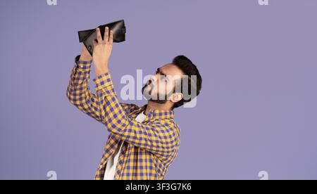 Concept de crise économique. Un homme indien contrarié avec un portefeuille vide sur fond violet Banque D'Images