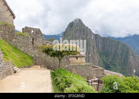 Vue des ruines anciennes en pierre de Machu Picchu avec des collines en terrasses et l'imposant mont Huayna Picchu sous un ciel nuageux à Cusco, Cusco, Pérou. Banque D'Images