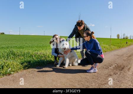 Groupe d'amis caressant un chien de Maremme lors d'une promenade à la campagne par une journée ensoleillée Banque D'Images
