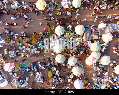 Vue aérienne d'un marché de plein air animé à Kimana avec des parasols colorés, des vendeurs et des acheteurs naviguant entre des étals remplis de produits frais Banque D'Images