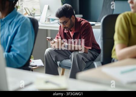 Homme indien adulte utilisant un smartphone pendant une pause au bureau Banque D'Images