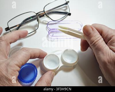 Les mains utilisent une pince à épiler pour manipuler des lentilles de contact à côté d'un étui à lentilles et de lunettes pour les soins oculaires quotidiens et le soutien de la vision Banque D'Images