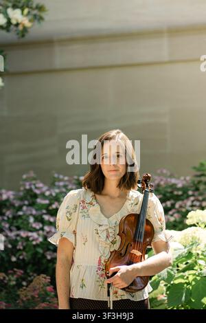 Femme avec un violon posant dans un jardin ensoleillé Banque D'Images