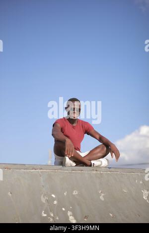 Jeune homme noir heureux se détendant en plein air contre un ciel bleu Banque D'Images