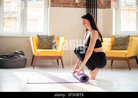Jeune femme en vêtements de sport déroulant son tapis de yoga Banque D'Images
