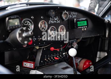 Vue intérieure détaillée d'un cockpit de voiture de course classique avec jauges analogiques, chronomètre numérique de tour, notes de stand écrites à la main et volant retiré Banque D'Images