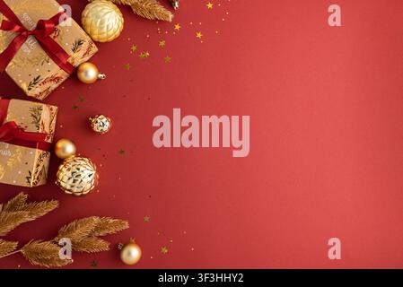 Boîtes cadeaux festives enveloppées dans du papier kraft avec des rubans rouges et des décorations dorées, comprenant des boules, des confettis en forme d'étoile et des branches de pin, créant un Holi riche Banque D'Images