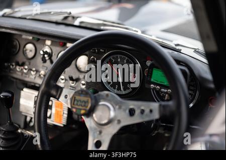Vue détaillée à travers le volant d'un tachymètre Stack sur le tableau de bord dans un cockpit de voiture de course classique. Banque D'Images