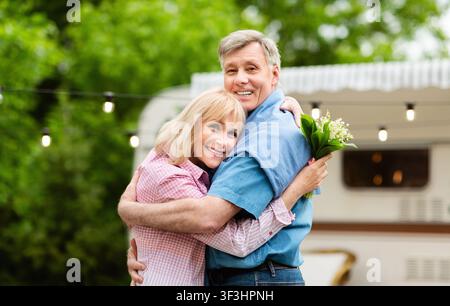Couple heureux et mûr avec bouquet de fleurs de champ enserre près de la remorque à l'extérieur Banque D'Images