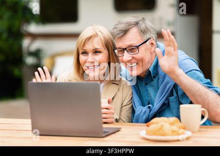 Joyeux homme âgé et sa femme communiquant avec sa famille ou ses amis sur un ordinateur portable au camping Banque D'Images