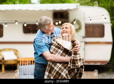 Homme senior attentionné couvrant sa femme bien-aimée avec une couverture près de motorhome sur le site de camping Banque D'Images