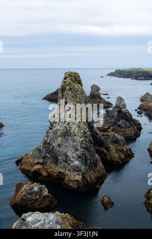 Des falaises marines robustes s'élèvent d'un océan bleu calme le long d'une côte rocheuse sous un ciel nuageux, évoquant la solitude, la beauté naturelle, l'érosion côtière et le drame Banque D'Images