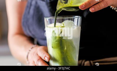 Une personne verse un thé matcha vif dans du lait froid avec des glaçons pour une boisson fraîche du matin Banque D'Images