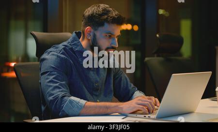 Homme d'affaires arabe concentré et sérieux travaillant avec un ordinateur portable dans un bureau du soir Homme indien surmené regardant l'écran Homme d'affaires hindou agent masculin Banque D'Images