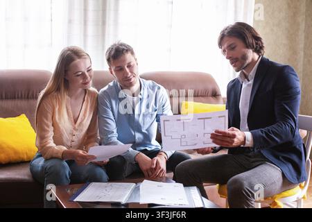 Directeur de l'établissement professionnel montrant le plan de la maison à un jeune couple à l'intérieur Banque D'Images