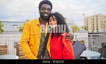 Portrait d'un homme afro-américain souriant avec une barbe et d'une femme caucasienne aux cheveux bouclés s'embrassant à l'extérieur. Couple heureux se tenant près l'un de l'autre Banque D'Images
