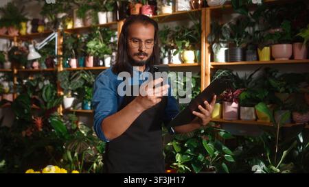 Portrait de face d'un jeune fleuriste caucasien supervisant des boutiques de fleurs en vérifiant des informations en ligne avec un smartphone. Beau jeune homme aux cheveux longs Banque D'Images
