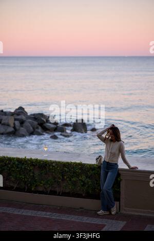Femme contemplant la mer debout le long d'un mur côtier Banque D'Images