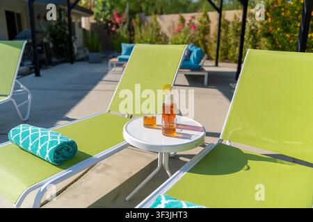 Thé glacé et carafe sur la table avec des chaises longues de patio. Chaises longues vert citron et une table blanche. Banque D'Images
