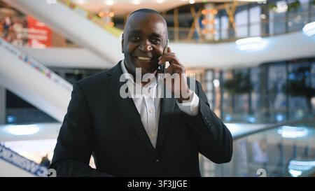 Homme d'affaires afro-américain mûr souriant, parlant au téléphone portable, discutant des tâches de travail dans un centre commercial, homme d'affaires d'âge moyen, employé, entrepreneur Banque D'Images