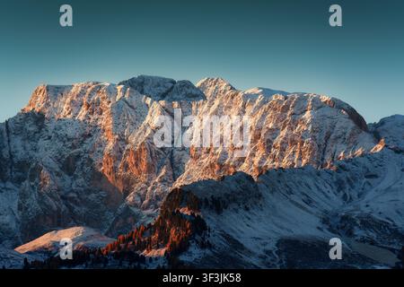 Sommetes majestueux des Dolomites enneigés baignés dans un chaud lever de soleil doré contre un ciel bleu avec des mélèzes d'automne dans un paysage alpin hivernal à It Banque D'Images