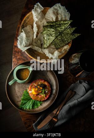 Vue aérienne d'une tartare de bœuf gastronomique avec jaune d'œuf, caviar et crackers de riz dans des assiettes en céramique. Banque D'Images