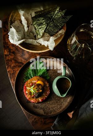 Vue aérienne d'une tartare de bœuf gastronomique avec jaune d'œuf, caviar et crackers de riz dans des assiettes en céramique. Banque D'Images
