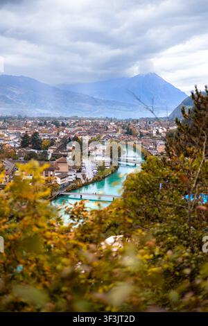 Vue du mont Harder Kulm surplombant la ville d'Unterseen avec la rivière Aare, entourée d'arbres d'automne et de montagnes sous un ciel nuageux à Unt Banque D'Images
